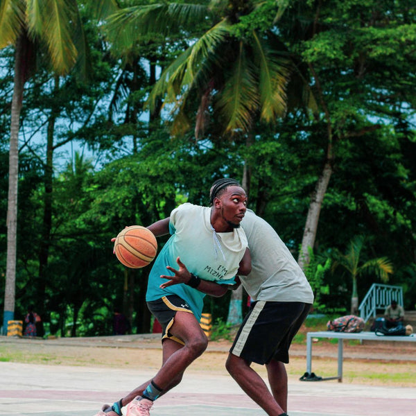 Two men playing basketball on an outdoor court with palm trees in the background