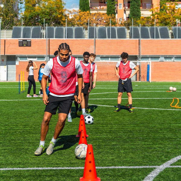 Soccer players practicing drills with cones and balls on a field.